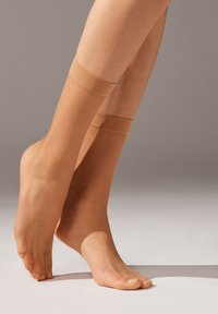 Beige, gennemsigtige strømpebukser med en glat tekstur og elastiske bånd foroven. Designet til at dække fødder og underben.