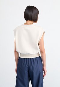 Ärmlös creamfärgad topp med ribbade kanter, matchad med löst sittande marinblå byxor. Tyget är slätt med en avslappnad passform och minimala detaljer.