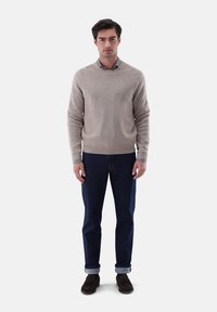 Beiger Strickpullover mit Rundhalsausschnitt, kombiniert mit dunkelblauen Jeans, hochgekrempelten Ärmeln und braunen Wildlederschuhen. Schlichtes Design, weicher Textil.