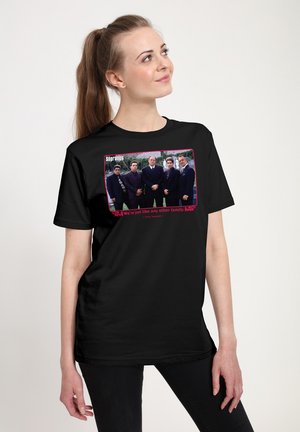 Kvinde iført sort t-shirt med gruppefoto af fem mænd i jakkesæt og teksten "The Sopranos" og et citat nedenunder.