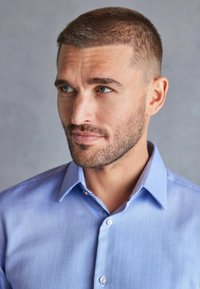 Lichtblauw overhemd met Visgraatpatroon en een button-down kraag. Beschikt over een subtiele textuur en contrasterende knoopaccenten.