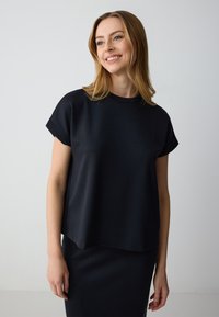 Top nero a maniche corte con scollo rotondo, realizzato in tessuto morbido. Il design presenta una vestibilità comoda e un orlo leggermente curvo.