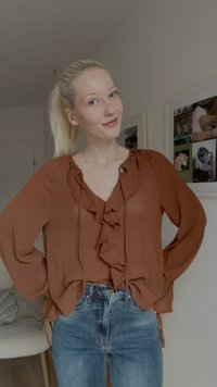 Blouse marron à manches longues avec des détails en volants au niveau du col, associée à un jean en denim bleu clair et un simple collier en argent.