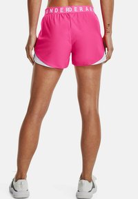 Rosa träningsshorts med vit kant, elastisk midja med texten "UNDER ARMOUR", och ett mjukt, lätt material.