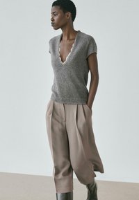 Grijs gebreid shirt met korte mouwen en een gerafelde V-hals, gecombineerd met beige broek met wijde pijpen en zwarte kniehoge laarzen; minimalistisch ontwerp.