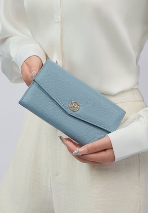 Portafoglio in pelle strutturata di colore azzurro chiaro con un accento in oro e chiusura a soffietto, tenuto in una mano, con una superficie liscia e bordi puliti.