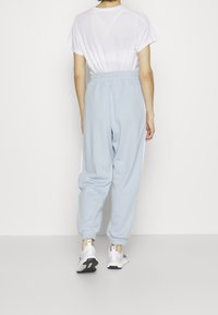 Pantalons de survêtement bleu clair avec une taille élastique, des poignets resserrés et des bandes blanches sur les côtés, associés à un t-shirt blanc uni et des baskets.