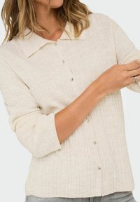 Cremfarbener, gerippter Button-Up-Shirt mit spitzem Kragen, Dreiviertelärmeln und seitlichen Schlitzen. Verfügt über kleine, runde Knöpfe und eine weiche Textur.