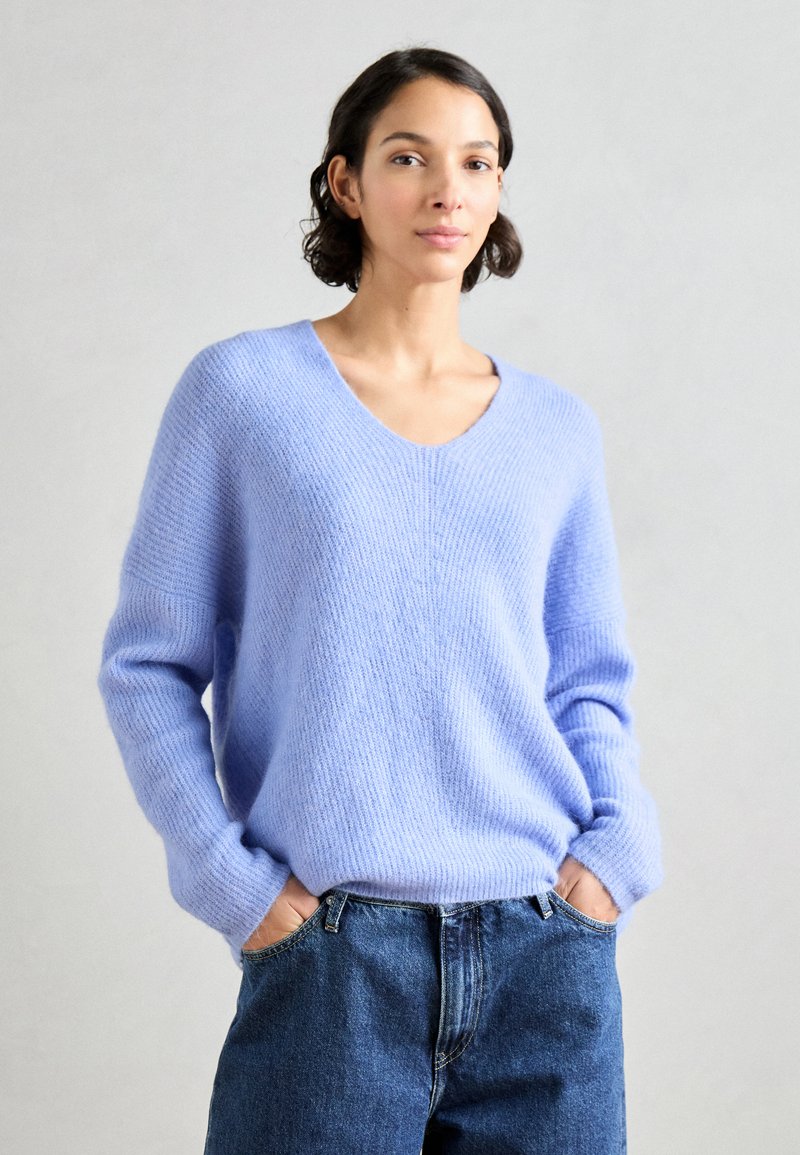 Lichtblauwe, comfortabele gebreide trui met een V-hals, lange mouwen en een ribbeltextuur, gecombineerd met hoog-zittende denimspijkerbroek.