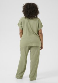 Top oversize color verde oliva con maniche corte abbinato a pantaloni coordinati. Tessuto morbido e leggero con una silhouette rilassata.