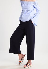 Jasnoniebieska bluzka z odkrytymi ramionami z marszczonym dekoltem, granatowe szerokie spodnie, oraz wielokolorowe klapki w paski.