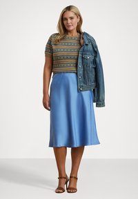 Strikket kort genser med flerfargede mønstre, kombinert med en lys blå sateng midi-skjørt og en denimjakke lagt over den ene skulderen.