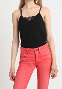 Svart satinlinne med spetsteknikk, parat med ljusrosa denimjeans. Linne har tunna axelband och en avslappnad passform.