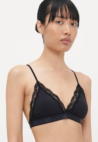 Zwarte bralette met kant langs de halslijn en randen, met dunne verstelbare bandjes en een gladde stof.