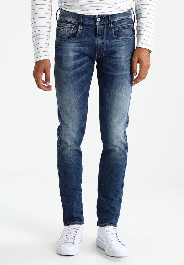 Mörkblå denimjeans med slim fit, ljus blekning framtill, klassiska fickor och knappstängning, som bärs med vita sneakers.