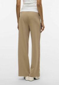 Beige wijde broek van gladde stof, met witte zijkanten en een ontspannen pasvorm. De zoom valt net boven de schoenen.