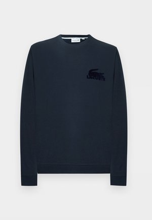 Sötét tengerészkék hosszú ujjú, kerek nyakú pulóver bordázott mandzsettákkal és egy kis fekete Lacoste krokodil logóval a bal mellrészen.
