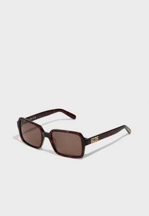 Brown tortoiseshell sunglasses with rectangular lenses, featuring gold "GCDS" branding on the temple. Sleek, modern design with a glossy finish.
