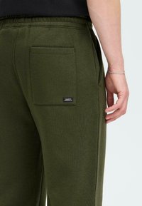 Olivgrüne Jogginghose aus weichem Material, mit einer einzelnen Gesäßtasche und einem elastischen Bund für zusätzlichen Komfort.