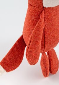 Orange plush toy with a textured finish, featuring a rounded body, long arms, and a tail. The feet have a contrasting light color detail.