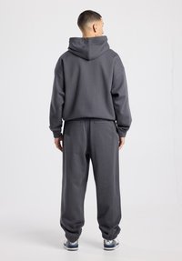 Grijze hoodie met een ontspannen pasvorm en een grote capuchon, gecombineerd met bijpassende grijze joggers met elastische boorden en zijzakken. Casual schoeisel maakt de look compleet.