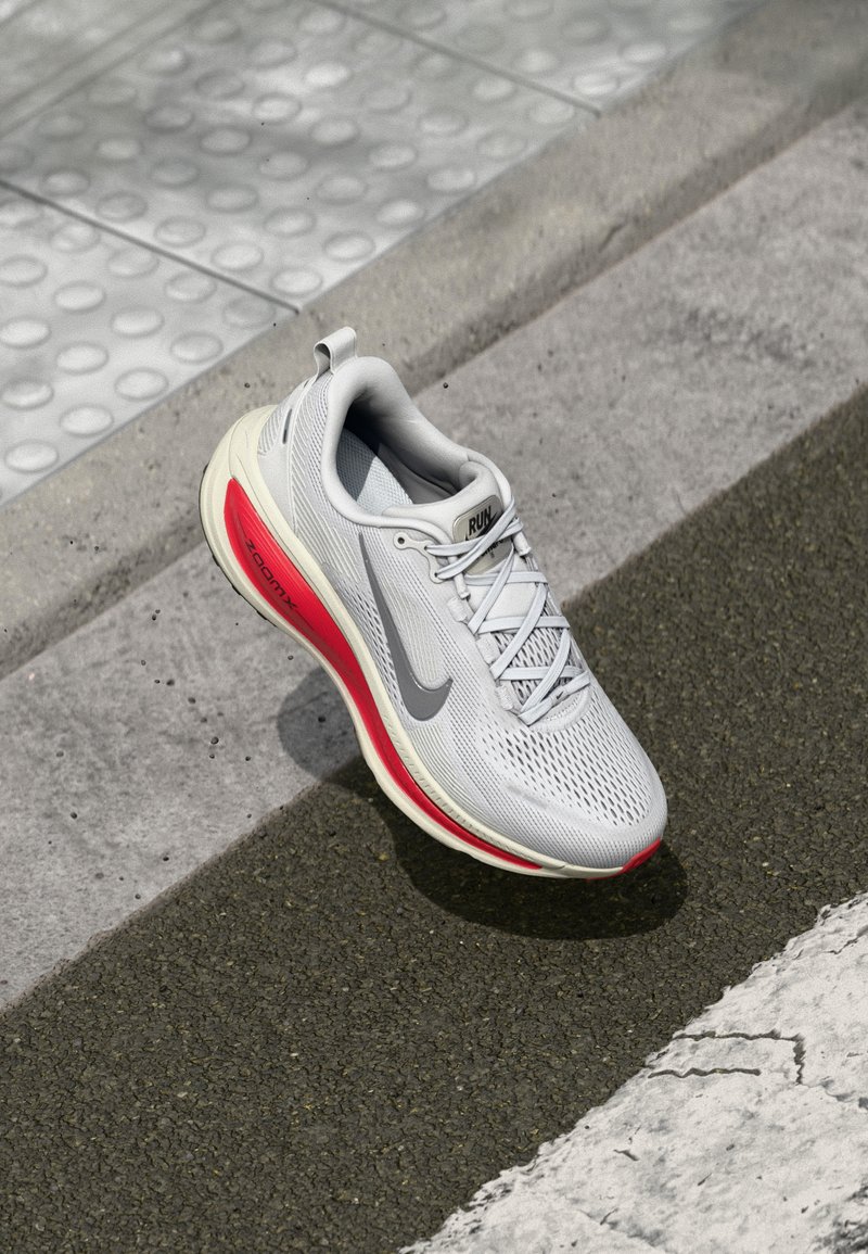 Chaussure de course pour homme en gris clair, avec une tige en mesh respirant, des accents rouges sur la semelle, un logo Nike réfléchissant et un col rembourré.