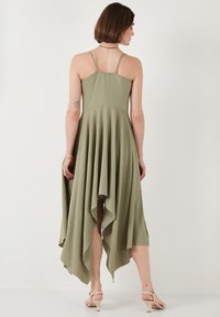 Olive green, sleeveless dress with a fitted bodice and asymmetric, flowing hem. Textured fabric with a relaxed silhouette and adjustable straps.