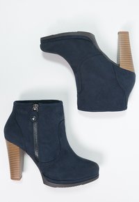 Bottines en daim bleu marine avec une fermeture éclair latérale, une forme profilée et un talon empilé marron. Équipées d'une semelle en caoutchouc pour une meilleure adhérence.