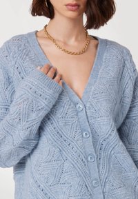 Helles blaues gestricktes Cardigan mit einem strukturierten Muster, tiefem V-Ausschnitt und Knopfverschluss, mit gerippten Bündchen und detailliertem Strick.