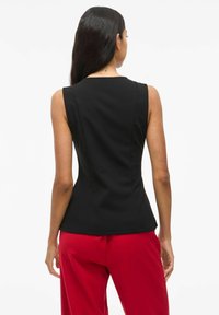Svart ärmlös topp med en figurnära design, slät textur och subtila sömmar, tillsammans med röda vida byxor.