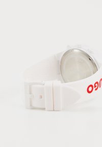 White silicone wristwatch with a round silver metal case, featuring red "HUGO" branding on the strap and a textured strap surface.