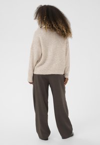 Bež svijetlosiva džemper s opuštenim krojem, teksturiranom tkaninom i širokim rukavima, u kombinaciji s smeškim, širokim hlačama. Outfit ima ležeran, opušten izgled.