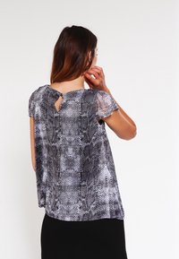 Blusa a manica corta con stampa serpente bianca e nera, caratterizzata da un'apertura a chiave sul retro e un tessuto fluido e leggero.