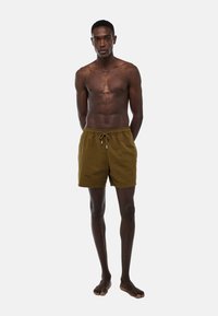 Shorts de bain marron texturé avec taille à cordon de serrage, coupe à mi-cuisse et coupe décontractée ; le mannequin est pieds nus avec une posture droite.