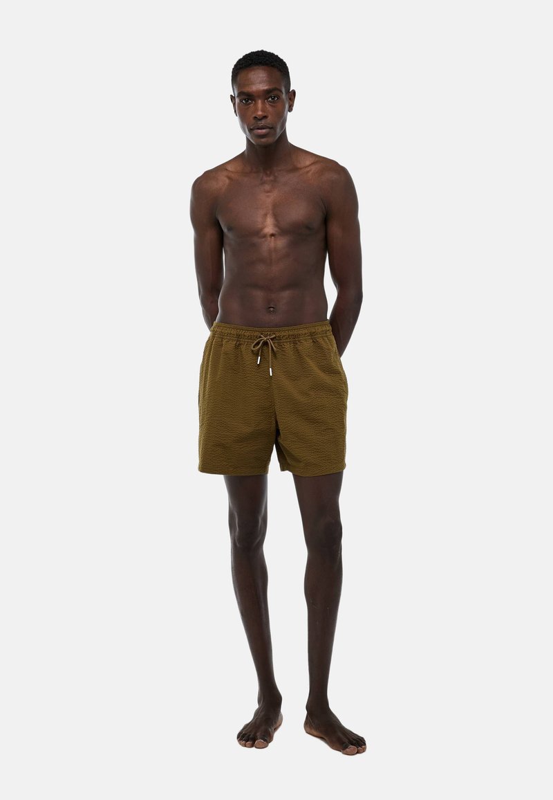 Shorts de bain marron texturé avec taille à cordon de serrage, coupe à mi-cuisse et coupe décontractée ; le mannequin est pieds nus avec une posture droite.