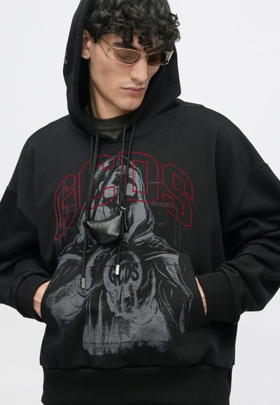 Hanorac negru cu glugă și inscriptionat cu litere roșii "GCDS"; dispune de o printare grafică cu o figură cu glugă. Include caiete de strângere și un buzunar frontal.