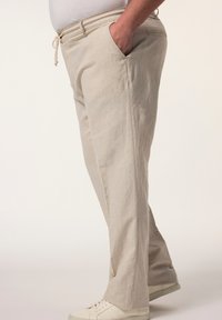 Helle beige Leinenhose mit lockerer Passform, ausgestattet mit Seitentaschen und einem Kordelzugbund, kombiniert mit weißen Sneakers.