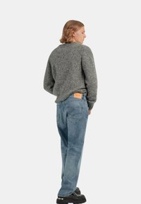 Maglione grigio testurizzato con scollatura rotonda, abbinato a jeans azzurri larghi. Scarpe con plateau nere e una targhetta in pelle sulla cintura.