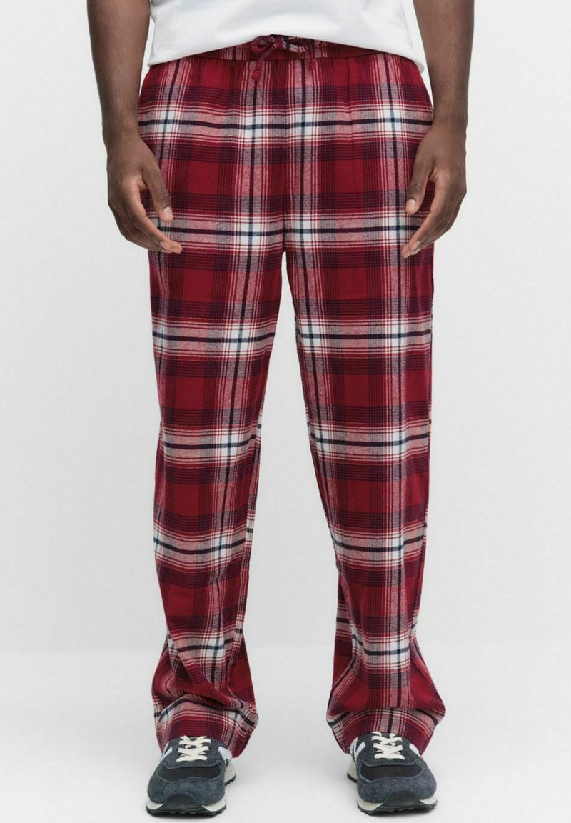 Rood en zwarte geruite pyjamabroek met een zachte textuur, verstelbare tailleband en een losse pasvorm. Gecombineerd met grijze sneakers en witte veters.