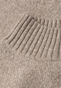 Gros plan sur un tissu tricoté beige avec des sections côtelées et lisses montrant des points détaillés.