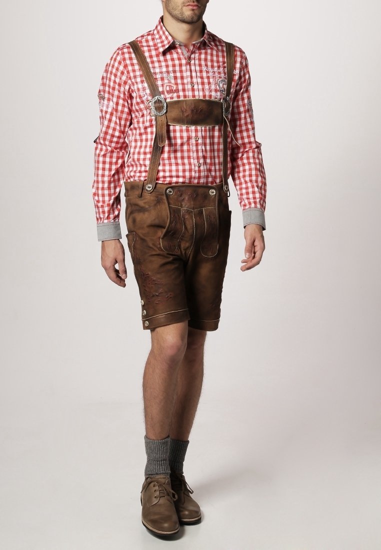 Lederhosen de cuero marrón con costura decorativa, camisa de cuadros rojos y blancos de botones, puños de suéter grises, calcetines grises y zapatos marrones.