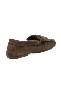 Mocasines de ante marrón con punta redondeada, detalle de cordones y suela plana de goma. Textura suave con acentos cosidos a lo largo de los bordes.
