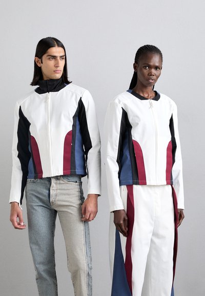 White jackets with black, blue, and maroon accents. Smooth fabric, zip closure, cropped design. Light denim and white pants complete the outfits.