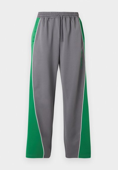 Γκρι φόρμα με πλατιά πράσινη πλαϊνή λωρίδα και λευκή περιμετρική ραφή, ελαστική μέση με κορδόνι και διακριτική γραπτή λεπτομέρεια στο δεξί μηρό.