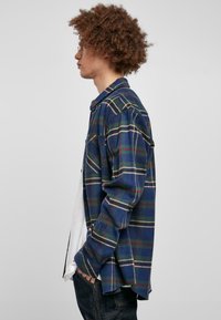Blå og grønn rutete flanellskjorte med krage og knapper, med lange ermer og løs passform, båret over en hvit t-skjorte.