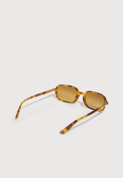 Lunettes de soleil rectangulaires en écaille de tortue marron avec des verres teintés marron, reposant sur une surface blanche.