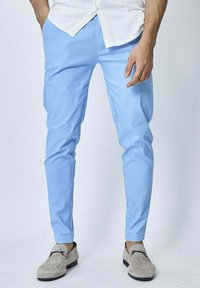 Pantalons ajustés bleu clair en tissu lisse, présentant un design de jambe fuselée, portés avec des chaussures gris à enfiler et une chemise blanche à boutons.