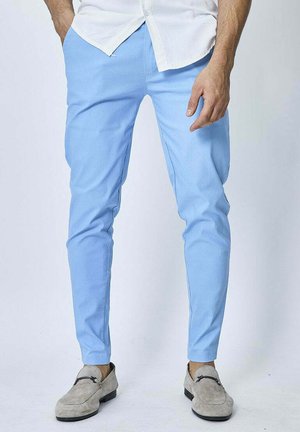 Pantalons ajustés bleu clair en tissu lisse, présentant un design de jambe fuselée, portés avec des chaussures gris à enfiler et une chemise blanche à boutons.