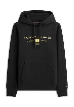 Sweat à capuche noir avec poche avant, capuche à cordon de serrage, et texte ainsi que logo dorés "Tommy Hilfiger American Classics Est. 1985" sur la poitrine.