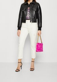 Chaqueta de cuero negra corta con puños acanalados, camiseta con estampado gráfico, jeans rectos blancos desgastados y un bolso de peluche rosa con cadena de oro.